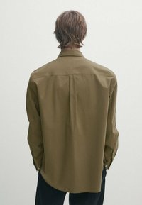 Olivengrünes Langarmhemd mit spitzem Kragen, geknöpften Manschetten und abgerundetem Saum. Aus glattem Stoff mit einer lockeren Passform gefertigt.