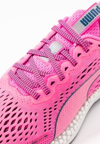Scarpa sportiva rosa con tomaia in mesh dal design testurizzato, dettagli in gomma e suola ammortizzata. Include lacci intrecciati e logo sulla linguetta.