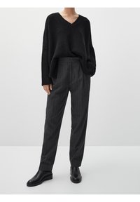 Czarny, oversize sweter dzianinowy z dekoltem w serek; zestawiony z ciemnoszarymi spodniami w prążki i czarnymi skórzanymi botkami za kostkę.