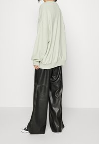Felpa oversize verde chiaro e pantaloni wide-leg neri in ecopelle. Sneakers bianche con dettagli neri completano l'outfit.