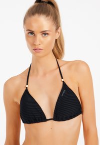 Top de bikini negro con textura acanalada, de forma triangular, con tirantes ajustables y detalles en dorado en el cuello. Logotipo de la marca visible.