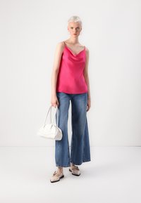 Rosa satengcamisole med en drapert nakke, kombinert med vide denimjeans. Tilbehør med en liten hvit håndveske og lyse sko.