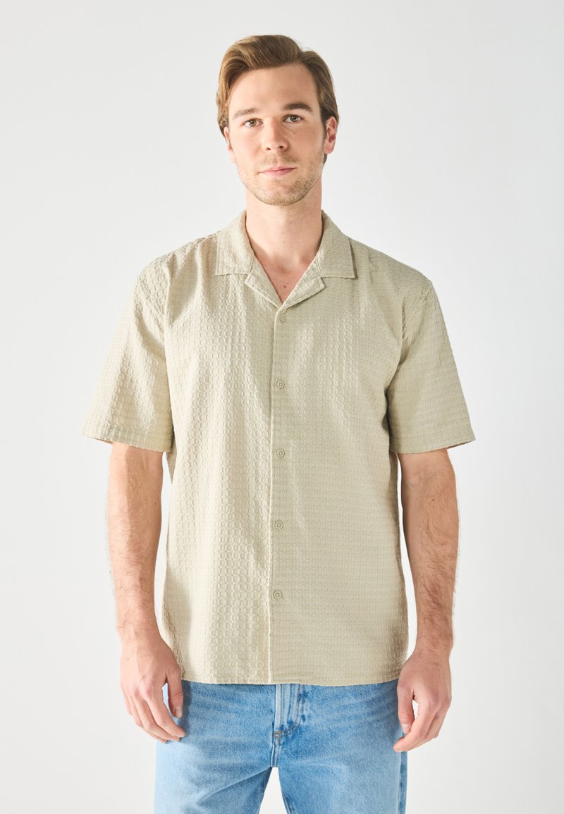 Korte mouwen overhemd met knopen in lichtbeige tekstuurstof, met een platte kraag en een relaxte pasvorm, gecombineerd met lichtblauwe denim jeans.
