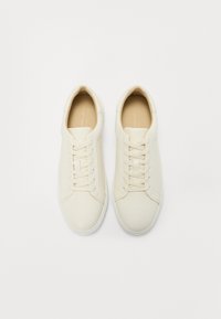 Baskets en cuir blanc avec une texture lisse, dotées d'une semelle plate, d'un bout arrondi et d'un design à lacets avec de subtils détails de couture.