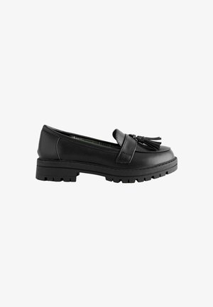 Mocassin en cuir noir avec semelle épaisse et pampilles décoratives à l'avant, montré de profil sur fond blanc.