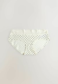 Sous-vêtements blancs pour femmes avec des pois noirs et une large ceinture en dentelle, posés à plat sur un fond clair.