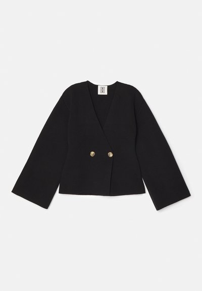 Melna divrindas žakete ar V veida kaklu, platām piedurknēm un diviem zelta pogām. Izgatavota no teksturēta auduma, ar saīsinātu apakšu.