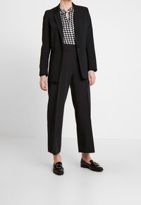 Sort blazer, bluse med hundetandsmønster, højtaljede sorte bukser og sorte loafers med cirkulært hardwaredetalje.