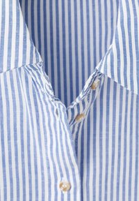 Col de chemise à rayures verticales bleues et blanches avec des boutons beiges partiellement boutonnés.