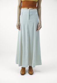 Jupe longue, bleu pâle, en tissu doux, avec un bouton avant et des poches latérales, associée à des chaussures brown à lacets.