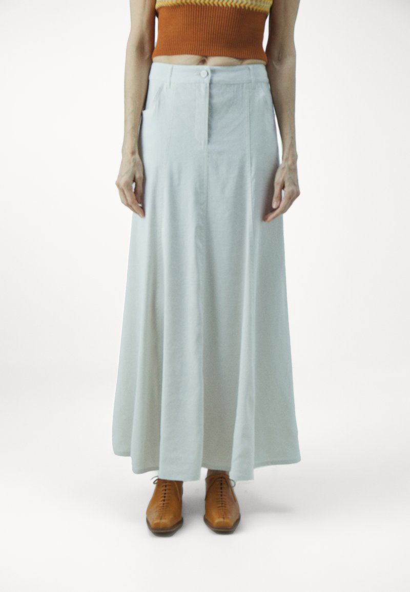 Jupe longue, bleu pâle, en tissu doux, avec un bouton avant et des poches latérales, associée à des chaussures brown à lacets.