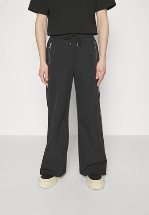 Pantalones anchos negros hechos de tejido ligero. Cuenta con dos bolsillos con cremallera y cintura con cordón ajustable. Se combinan con zapatos de plataforma informales.