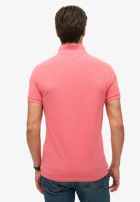 Camisa polo de manga corta en un vibrante tejido color coral. Presenta un cuello clásico y una textura suave, combinada con unos vaqueros.