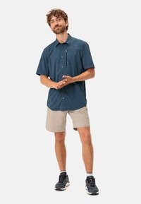 Camisa de manga corta de botones en azul oscuro con un patrón de cuadrícula, combinada con pantalones cortos beige. Cuenta con un bolsillo en el pecho y una tela ligera.