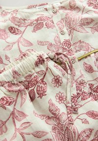 Țesătură moale crem cu modele florale roz, cu nasturi în față și talie elastică cu șnur legat.