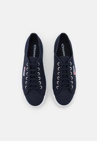 Paire de baskets en toile bleu marine avec semelles en caoutchouc blanches et lacets noirs, arborant le logo "Superga" sur le côté et la semelle intérieure, vue de dessus.