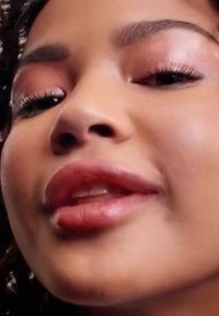 Close-up of a face with plump lips, subtle gloss, dark eyelashes, and a smooth complexion. Skin tone appears warm, with defined cheekbones.