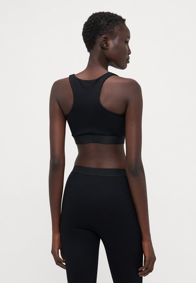 Sort sports bh med racerback-design, glat stof og en støttende elastisk bånd i bunden. Båret sammen med matchende sorte leggings.