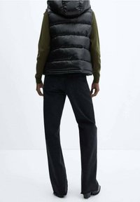 Czarna pikowana kamizelka z kapturem na zielonej bluzce z długim rękawem, zestawiona z czarnymi szerokimi jeansami. Gładka faktura, casualowy design.