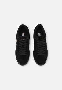 Sneakers in suede nero con fodera in pelliccia sintetica, stringhe nere piatte, suola in gomma e piccolo logo dorato laterale. Design classico a scarpa bassa.