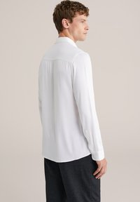 Biela košeľa s dlhým rukávom z ľahkej tkaniny, s klasickým golierom, zapínaním na zapínanie a zaobleným lemom.