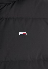 Black puffer jacket fabric with horizontal quilted pattern. Features a small embroidered logo in white, red, and blue near the center.