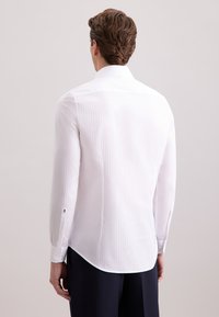 Wit gestreept shirt met lange mouwen, taillerend figuur, gebogen zoom en knoopmanchetten. De stof heeft een gladde textuur en een subtiele glans.