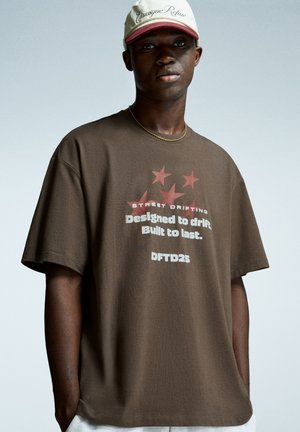 Brun bomulds t-shirt med et grafisk design med stjerner og teksten "STREET DRIFTING" samt "Designed to drift. Built to last. DFTD25."