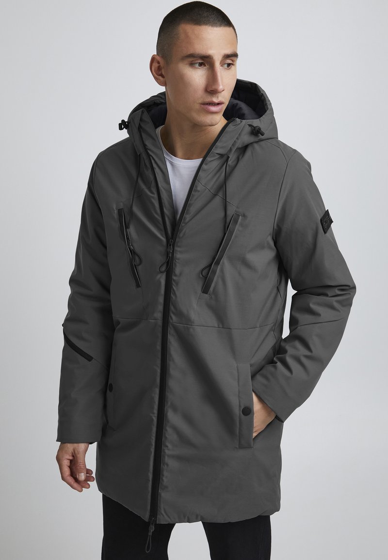 Parka grise à capuche dotée d'une fermeture éclair, de deux poches à l'avant et d'accents ton sur ton. Fabriquée en matériau lisse et résistant à l'eau.