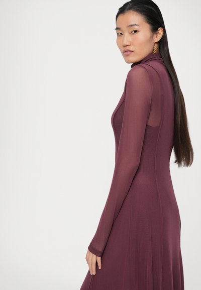 Vestito malva con maniche lunghe e trasparenti e collo alto; corpino aderente che passa a un orlo svasato, che mette in mostra un tessuto texturizzato.