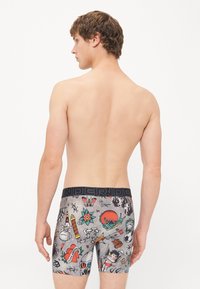 Männer Boxershorts aus grauem Baumwollstoff mit bunten Tattoo-ähnlichen Druckmotiven. Ausgestattet mit einem schwarzen, gebrandeten Elastikbund und einer figurnahen Passform.