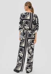 Navyblauer Jumpsuit mit weißen Blättermustern, weitem Hosenbein, elastischem Bund und lockeren Ärmeln, aus einem Stoff mit subtiler glänzender Textur.