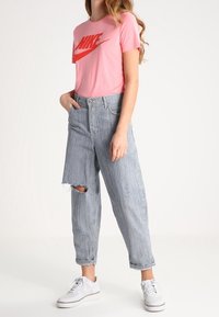 Ljusrosa T-shirt med röd Nike-logotyp, tillsammans med ljusblå, slitna jeans och vita sneakers. Avslappnad stil med uppvikt ärm.