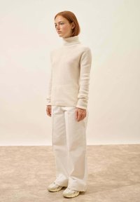 Kremowy sweter z golfem i prążkowaną fakturą, zestawiony z białymi spodniami o szerokich nogawkach i beżowymi trampkami; gładka tekstura i dopasowany krój.