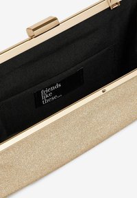 Gold glitter clutch with a hard shell, featuring a black fabric interior and a metallic clasp. Inside has a label with "friends like these...".