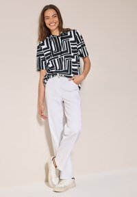 Camisa de manga corta con un patrón en blanco y negro, combinada con pantalones anchos blancos y zapatillas blancas, todo sobre un fondo neutro.