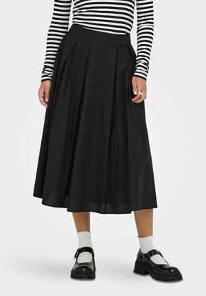 Jupe plissée noire avec une taille ajustée, fabriquée en tissu léger. Associée à des chaussures noires et des chaussettes blanches.