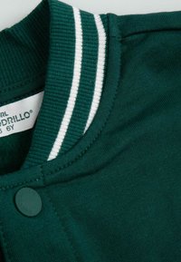 Ciemnozielona bluza z prążkowanym kołnierzem, ozdobiona białymi paskami, z zapięciem na napy oraz miękką fakturą materiału.