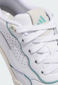 Vita sneakers med strukturerat läder, turkosa detaljer och perforerad design. Har vita skosnören och en grå mockatunga.