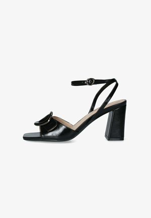 Sandale cu toc înalt din piele patent neagră, cu vârf deschis, brâu ajustabil la gleznă și un accent circular mare în față. Toc pătrat.
