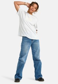 Camiseta corta de manga gris con un diseño gráfico en el pecho, combinada con unos vaqueros de pierna ancha azules y zapatillas negras.