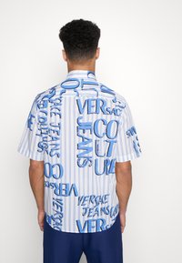 Kortärmad skjorta i blått och vitt med randiga mönster och djärva texttryck. Har en avslappnad passform, standardkrage och ett slätt tyg.