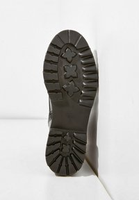 Suola di stivali in gomma nera con profonde scanalature, caratterizzata da motivi a forma di stella per la trazione, tacco leggermente curvato e bordi lisci.