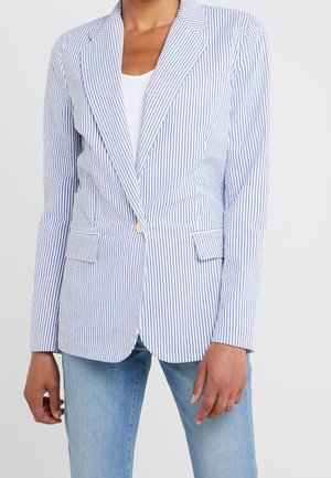 Person iført en lyseblå og hvide vertikale stribet blazer med en enkelt knap, kombineret med lyseblå jeans og en hvid top.