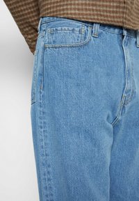 Vaaleansiniset farkut, joissa on suora lahje, viisi taskua ja näkyvät tikkaus yksityiskohdat. Tasainen rakenne ja klassinen malli.