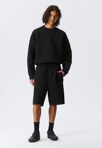 Schwarzer Fleece-Sweatshirt und passende Shorts mit einem Kordelzugbund. Glatte Textur, lässige Passform, knielange Shorts und keine sichtbaren Logos.
