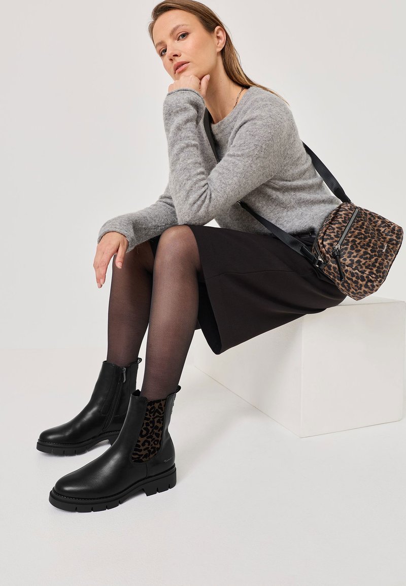Černé kožené kotníkové boty s elastickými panely v leopardím vzoru, texturovanou podrážkou, nošené s šedým svetr a černou sukní.