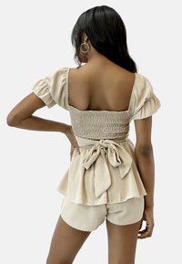 Beige Zweiteiler bestehend aus einem gerafften Oberteil mit Puffärmeln, einer Schleife am Taillenbund und passenden Shorts mit entspannter Passform.