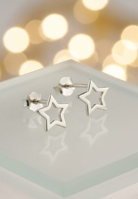 Sterlingsilver stjärnformade studs med en öppen design, placerade mot en mjuk, suddig ljusbakgrund som reflekterar deras form.