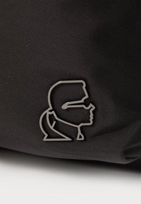 Crna torba s teksturiranom površinom i metalnim akcentom logotipa koji prikazuje profil dizajn. Izdržljiv, kompaktan, praktičan stil.